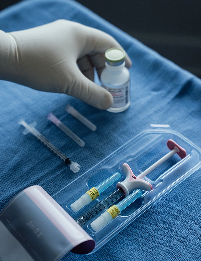 Gloved hand holding medical vial above organized tray of syringes and medical supplies on blue surgical drape - Botox and wrinkle relaxers in Parsippany, NJ.