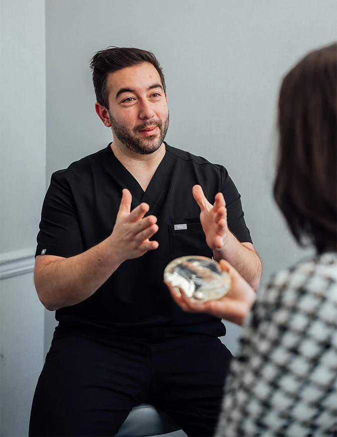 Healthcare professional in black scrubs consulting with patient, explaining treatment with hand gestures - Breast implant removal in Parsippany, NJ.