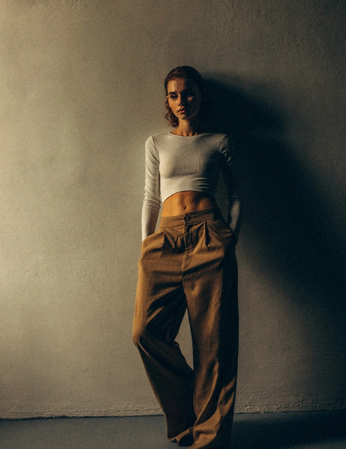 Woman in white crop top and tan wide-leg trousers posing against minimalist wall with dramatic shadow lighting - post ozempic in Parsippany, NJ.