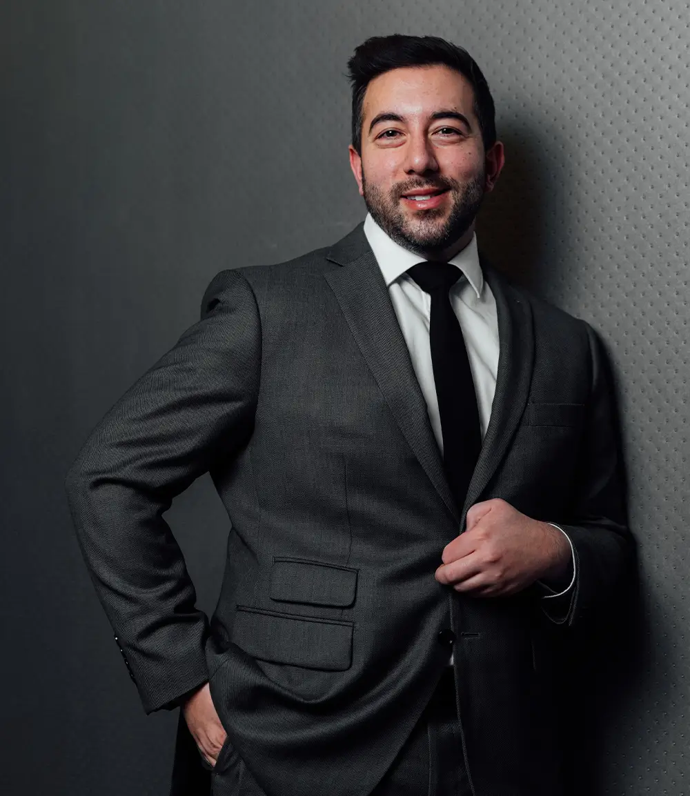 Doctor shuja in black suit and tie posing confidently against gray background