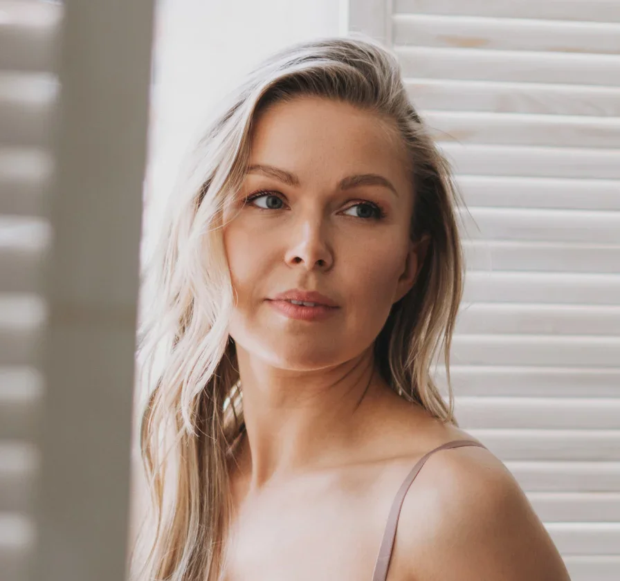 Woman with long blonde hair in natural light by window with white blinds - face fat transfer in Parsippany, NJ.
