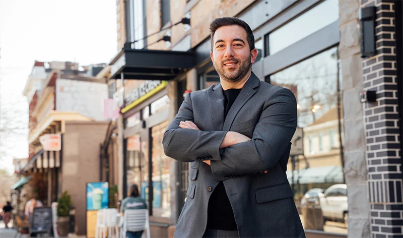 Doctor Shuja in suit standing confidently on urban street with arms crossed